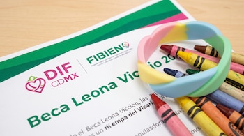 Hoja impresa Beca Leona Vicario 2026, logos DIF CDMX y FIBIEN, pulsera de silicona multicolor, y crayones de colores sobre escritorio de madera.