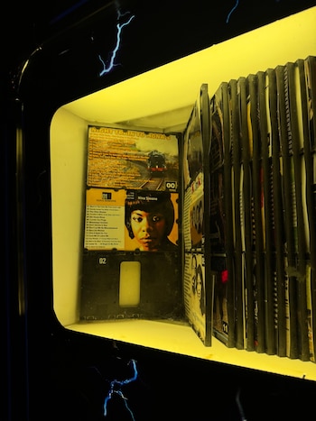 Interior iluminado de amarillo de una máquina de música que contiene carátulas y listas de canciones de discos compactos