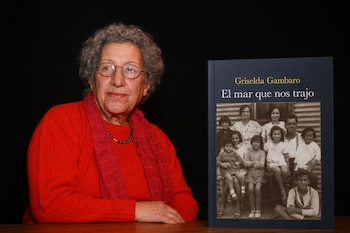 Una mujer con anteojos y prenda roja está sentada junto a la portada de un libro que exhibe una fotografía familiar.
