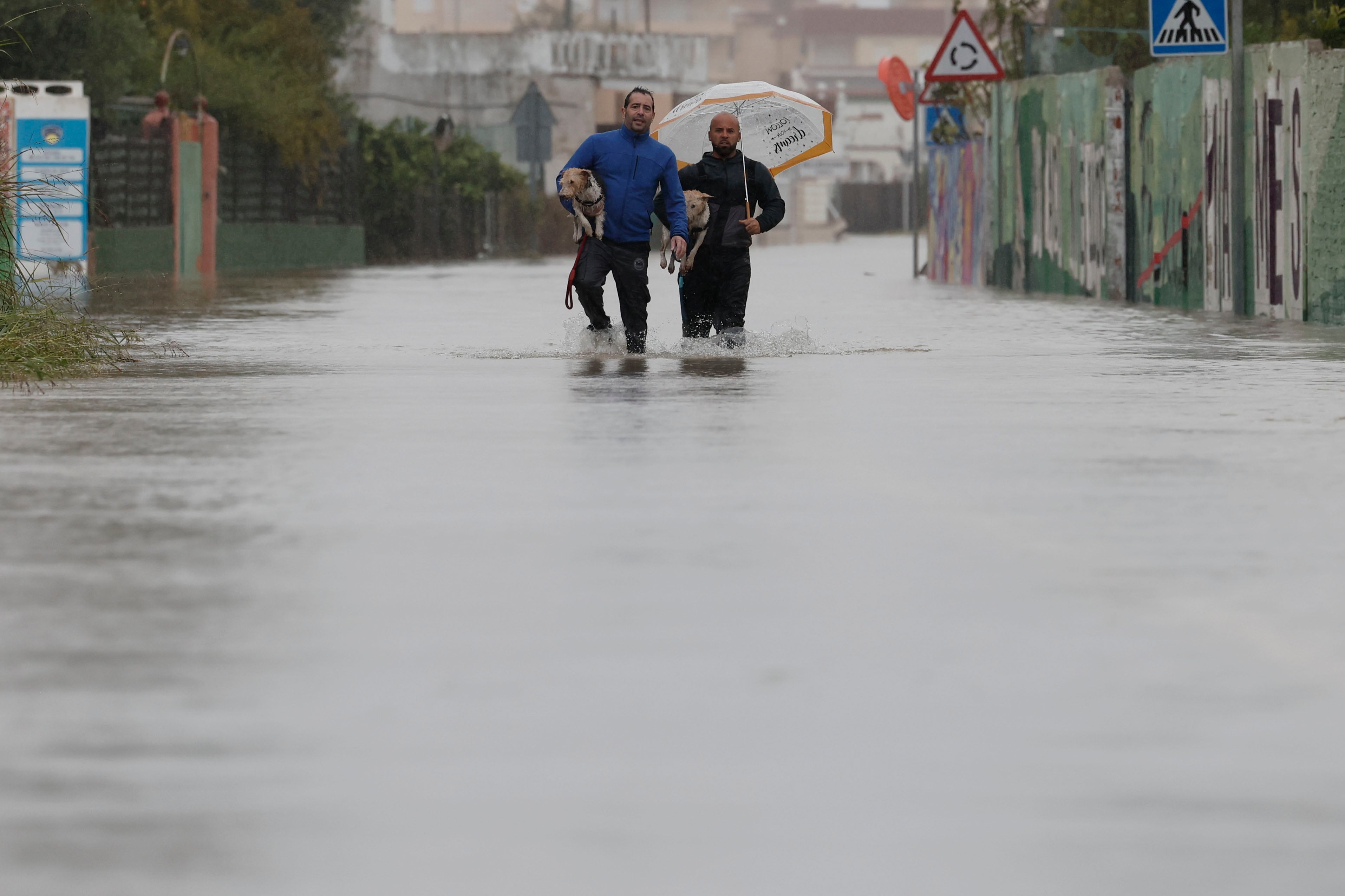 Dos personas abandonan con sus perros la zona de la playa de Bellreguard (Valencia) a través de una carretera inundada. (Manuel Bruque/EFE)