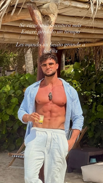 Un hombre con lentes de sol y camisa abierta sostiene un vaso bajo una estructura de madera y paja con un mensaje sobreimpreso en la parte superior