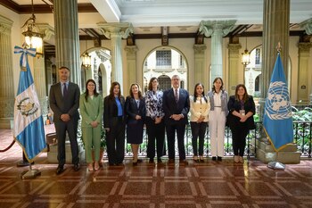 Diez personas, un hombre y nueve mujeres, posan en una fila entre las banderas de Guatemala y Naciones Unidas, en un vestíbulo con columnas