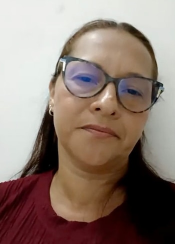 Una mujer con cabello castaño, anteojos y blusa roja posa frente a un fondo blanco