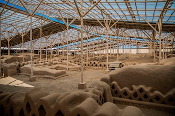 Techo de bambú y láminas translúcidas sobre estructuras de adobe antiguas, terreno de gravilla y fragmentos de cielo azul