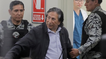 Alejandro Toledo camina escoltado por guardias con chalecos y camuflaje junto a personal médico en un pasillo interior