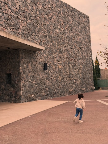 La hija menor de Darío Barassi caminando por el exterior de una iglesia de piedra, donde asistió a misa junto a su padre.