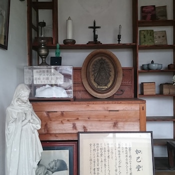 Estatua de la Virgen María, máscara póstuma en urna, relieve ovalado de la Virgen, cruz, vela, lámpara, libros, foto, texto en japonés, estantes de madera
