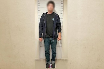 Un hombre con el rostro borroso viste una chaqueta oscura y pantalones azules frente a un medidor de estatura