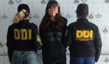 Una mujer con el rostro pixelado permanece custodiada por dos efectivas policiales frente a un fondo de la DDI Mar del Plata
