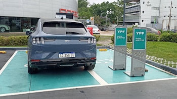 Un automóvil gris con patente argentina estacionado en un espacio verde junto a dos tótems de carga con el cartel YPF Punto Eléctrico