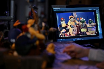 Un monitor que exhibe personajes en miniatura junto a figuras físicas desenfocadas en primer plano