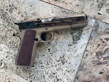 Pistola automática de color beige con corredera oscura y empuñadura de textura marrón sobre una superficie de baldosas