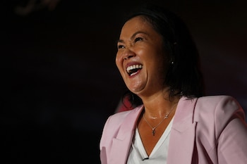 Primer plano de Keiko Fujimori sonriendo ampliamente, con sudor en su rostro y cuello. Viste un blazer rosa claro y un collar de cruz plateada