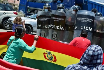 Agentes de policía hacen guardia frente a los manifestantes que bloquean una carretera con una bandera boliviana durante las protestas en Cochabamba (REUTERS/Patricia Pinto)