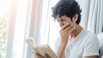 Un hombre aburrido lee un libro que parece no entretenerle -(Imagen Ilustrativa Infobae)