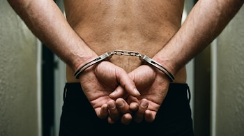 Las manos de un hombre están sujetas por la espalda con esposas metálicas.
