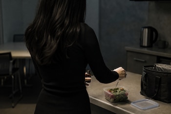 Una mujer vista de espaldas utiliza un gotero para aplicar un líquido en un recipiente con ensalada sobre una mesada de cocina.