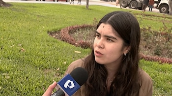 Una mujer joven de cabello oscuro habla frente a un micrófono con el logotipo azul de Panamericana Televisión en un área verde