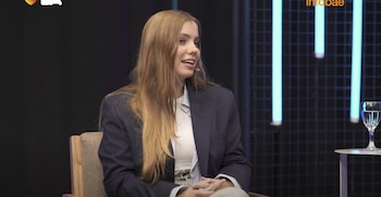 Florencia Andersen, una joven mujer rubia con blazer y camisa, sentada en una silla, hablando en un estudio con luces de neón azules