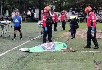 Un hombre con un saco azul y una corbata celeste está sentado en un sofá gris frente a una mesa de vidrio y una ventana