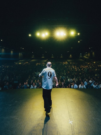 Un hombre en el escenario, de espaldas, vistiendo una camiseta con el número 9, frente a un auditorio lleno de personas aplaudiendo y luces brillantes