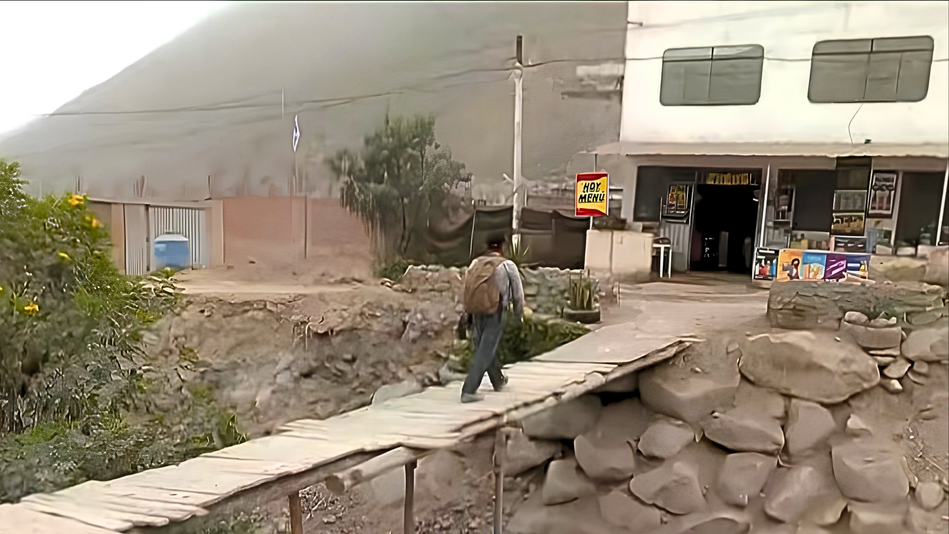 Un transeúnte cruza la quebrada California en Lurigancho-Chosica sobre un puente de tablas de madera sin barandas construido por los propios residentes. (Captura: Buenos Días Perú / Panamericana Televisión)