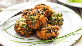 Un plato blanco con varios buñuelos dorados de acelga y queso, decorado con tallos verdes de cebollino.