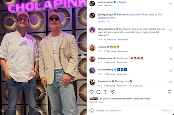 Dos hombres con gorras posan de pie delante de una pared con paneles metálicos y un letrero luminoso rosa que dice Chola Pink