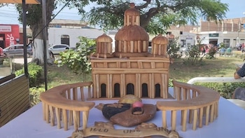 Estructura hecha con piezas de pan horneado sobre una mesa blanca, que figura un edificio con cúpula y columnatas en un parque público