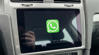Primer plano de una pantalla de infoentretenimiento de un carro con un borde plateado, mostrando el icono verde de WhatsApp sobre un fondo oscuro.