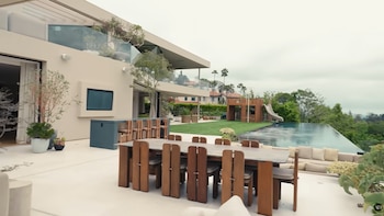 Fachada de edificio de varios niveles, balcón con vidrio, piscina de borde infinito, área de césped, mesa de comedor con sillas, bar exterior, sofás, juegos infantiles, árboles