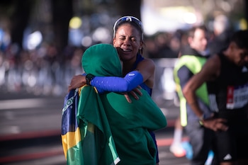 Una atleta vestida de azul abraza a una persona con capucha verde y la bandera de Brasil