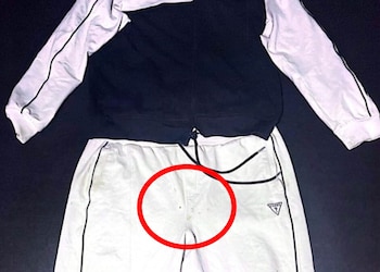 Un conjunto de jogging blanco y negro está estirado sobre una superficie oscura, mostrando una chaqueta negra y un pantalón blanco con manchas en la entrepierna