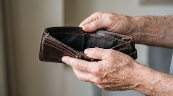 Manos de un hombre mayor sostienen una billetera de cuero marrón abierta y vacía con desgastes en los bordes.