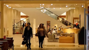 Interior de una tienda Nordstrom con clientes, exhibiciones de calzado, un letrero de "Service Bar" y una escalera mecánica