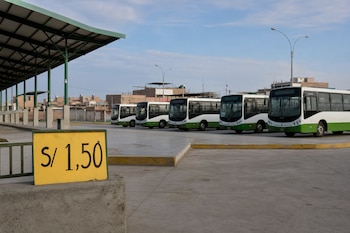 Cartel amarillo con el texto S/ 1,50 en primer plano y varios buses de color blanco y verde estacionados en una terminal vacía.