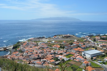 Vista elevada de un poblado costero con casas de tejados rojos, una pista de aviación junto al mar y tierra en el horizonte