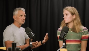 Spector, un hombre con cabello gris, y Amati, una mujer rubia, sentados con micrófonos de podcast delante, sobre un fondo negro. Spector gesticula