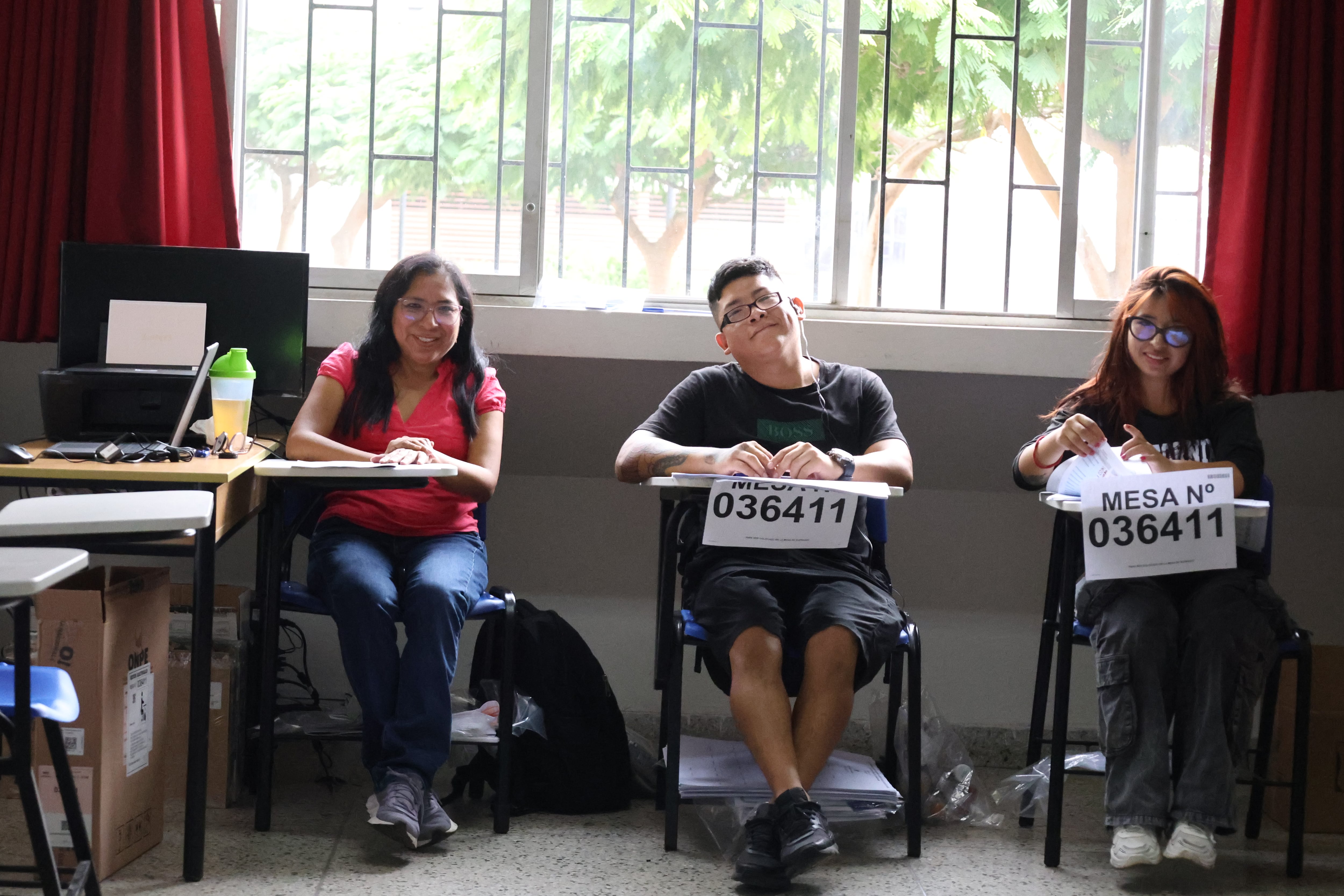 Tres personas sonrientes están sentadas en escritorios individuales con letreros