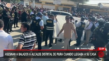 Agentes de policía y una multitud de personas se agrupan en una calle soleada alrededor de un sedán oscuro, mientras algunos sostienen una sábana blanca