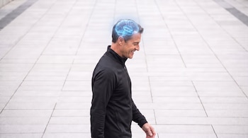 Hombre de perfil sonriendo con chaqueta negra. Un cerebro azul brillante y traslúcido con conexiones neuronales aparece sobre su cabeza.