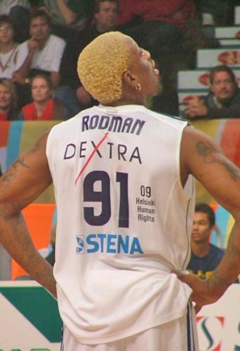 Un hombre de espaldas con cabello rubio teñido lleva una camiseta blanca de baloncesto con la palabra Rodman y el número 91