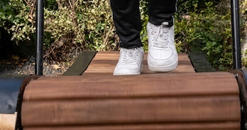Pies con zapatillas blancas y pantalón negro sobre los listones de madera de una cinta de correr curva