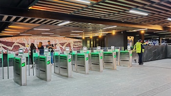 Interior de la Terminal Tasqueña del Metro CDMX remodelada. Se ven torniquetes modernos con luces verdes, un muro con mosaico y pasajeros. Un oficial de policía está a la derecha