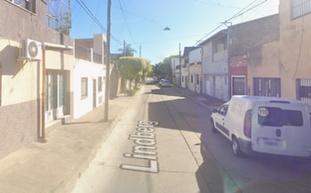Vista de una calle residencial con casas de plantas bajas, una camioneta blanca estacionada y la palabra Lindberg en el asfalto