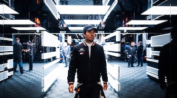 Un hombre con gorra y chaqueta camina por un pasillo con marcos de luz blanca brillante y paredes reflectantes.