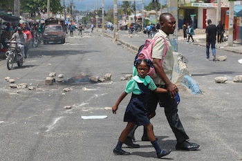 Dos residentes cruzan una avenida bloqueada con piedras por manifestantes durante una protesta para exigir la renuncia del consejo presidencial de transición, el 26 de marzo de 2025, en Puerto Príncipe, Haití (AP Foto/Odelyn Joseph)