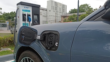Un vehículo gris con el puerto de carga abierto estacionado frente a un surtidor eléctrico de la empresa YPF