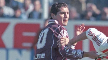 Primer plano de Hugo Morales, futbolista con camiseta número 10 granate y blanca, forcejeando con un oponente durante un partido