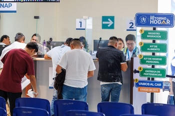 Personas de espaldas en un mostrador de servicio; se ven letreros de "Plan Retorno al Hogar", una flecha verde, y pasos de proceso numerados